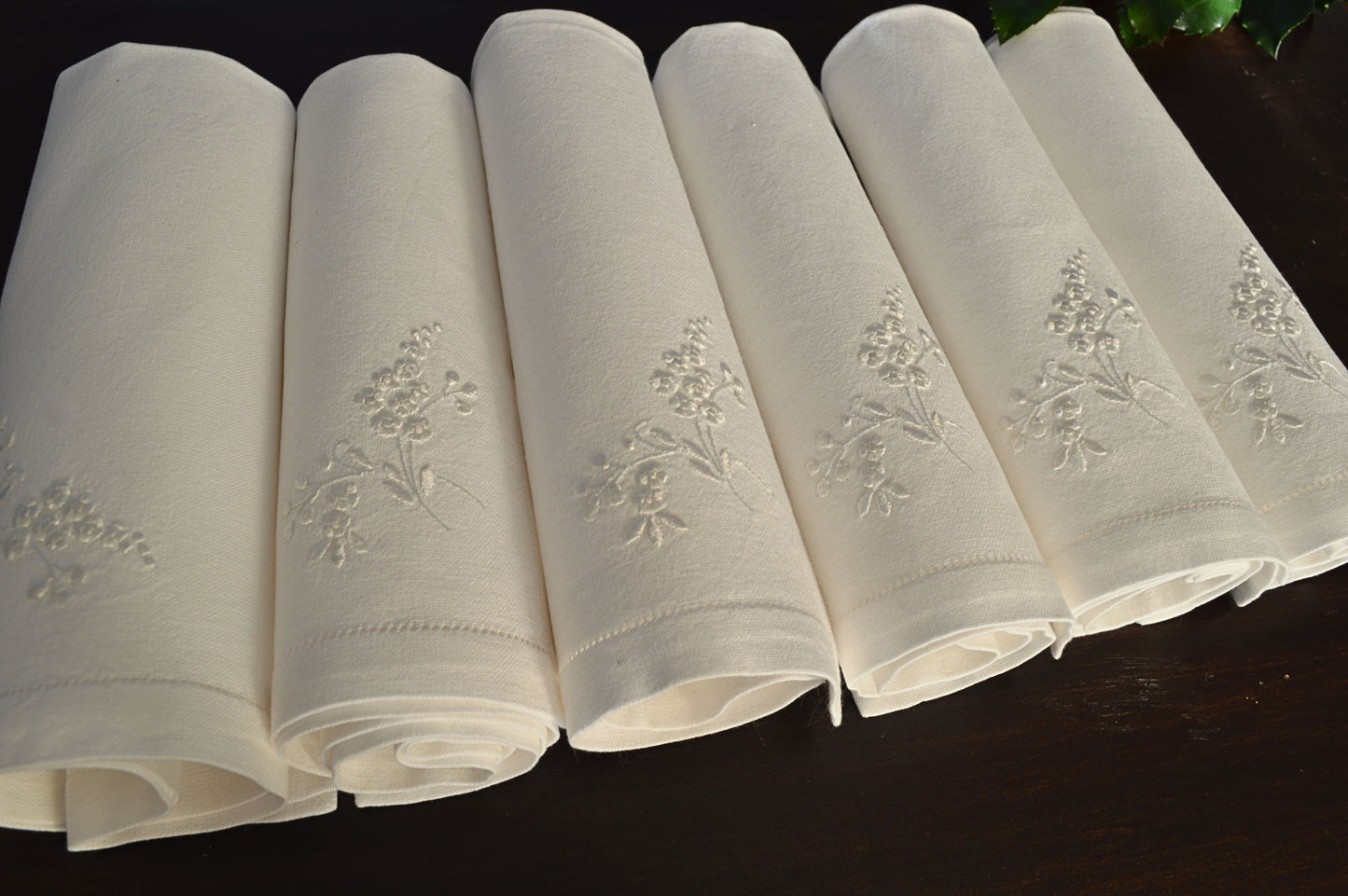 Set of six soft white cotton dinner napkins, rolled and displayed showcasing the fine white work hand embroidery work.